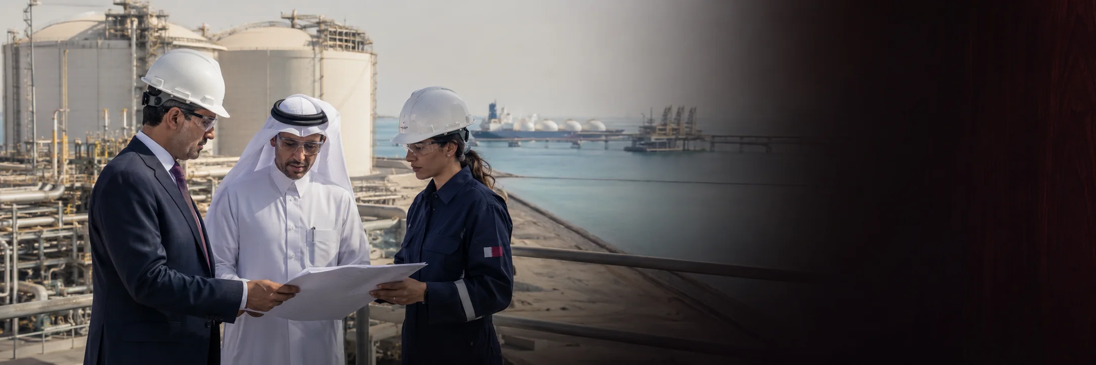 A Qatari lawyer and two engineers in safety helmets reviewing a drawing at a liquefied natural gas facility on the Qatari coast
