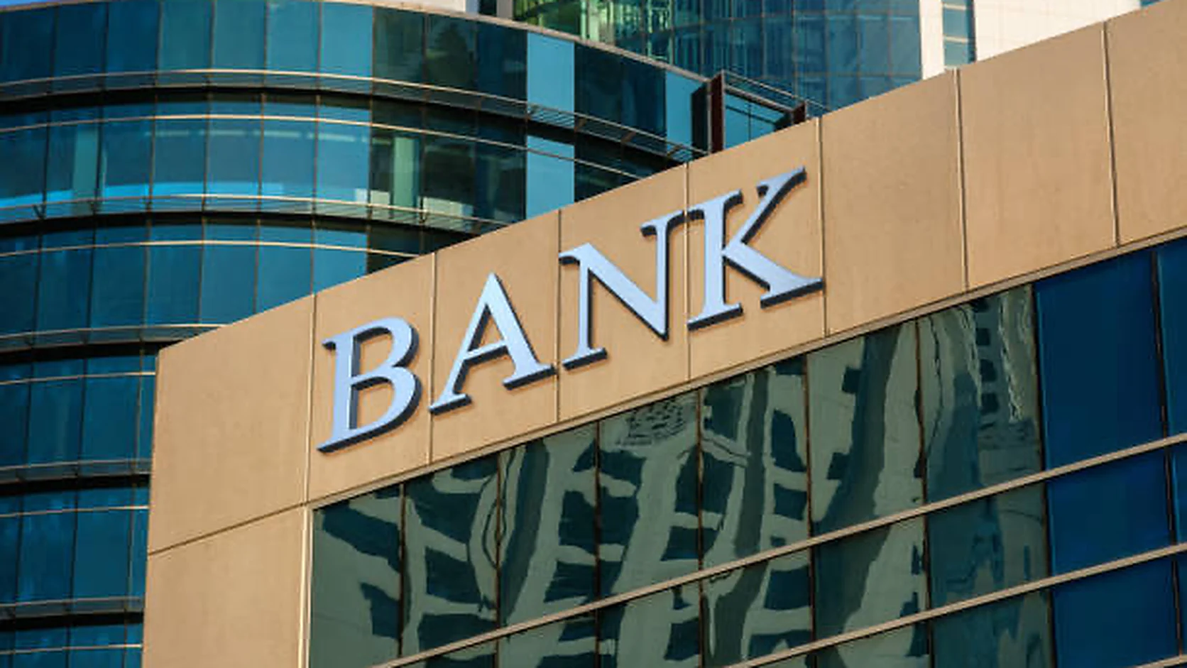 A bank building façade with a large "BANK" sign, glass tower reflections behind it.