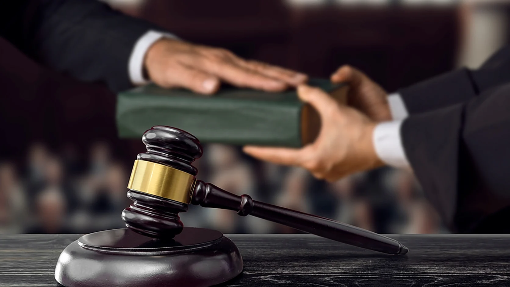 A judge handing down a bound legal volume to counsel across the bench, with a gavel resting on its sound block in the foreground.
